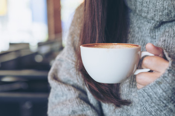 Closeup image of a woman holding white cup of hot coffee sitting in cafe in winter time