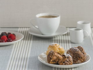 A dish of chou cream with a cup of tea or coffee and a dish of various berry for an afternoon break.