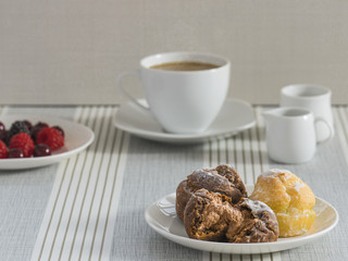 A dish of chou cream with a cup of tea or coffee and a dish of various berry for an afternoon break.