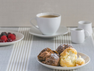 A dish of chou cream with a cup of tea or coffee and a dish of various berry for an afternoon break.