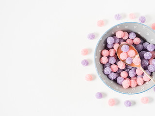 Round purple and pink bonbon candies sweets in gray bowl on white canvas background. Minimal still life