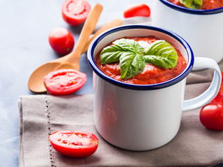 Creamy Tomato soup in enamel mugs on blue background