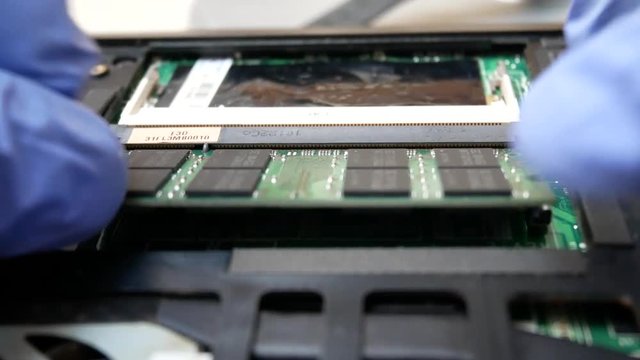 Hand in blue gloves installing ram dimm in notebook in the service center for repair and upgrade of computers or laptop