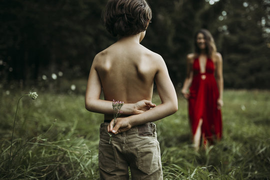 Shirtless son holding flowers behind back with mother in background