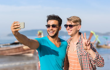 Man Tourists Couple Taking Selfie Photo In Front Of Long Tail Boat On Beach On Cell Smart Phone, Two Young Guys Happy Smiling On Sea Vacation