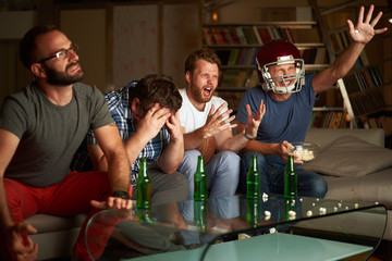 Four friends watching game of american footbal, showing frustration