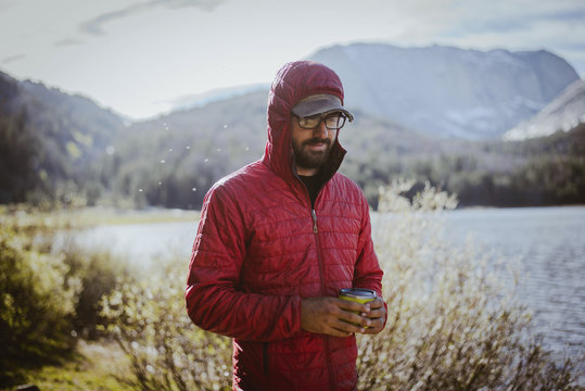 Hiker in hood holding drink can while standing by lake at Grand Teton National Park