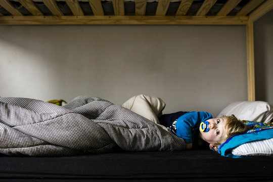 Portrait of boy sucking pacifier while lying on bed
