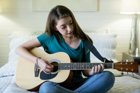 Teenage Girl Plucking Guitar In Bedroom