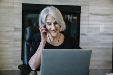 Smiling businesswoman answering smart phone while sitting in office