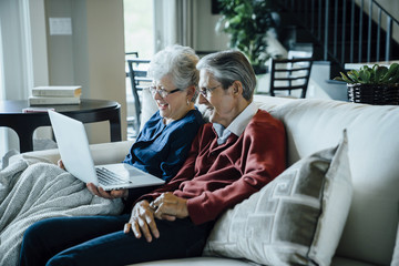 Senior couple video conferencing through laptop computer while sitting on sofa