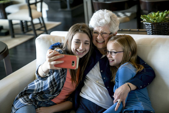 High angle view of happy grandmother and granddaughters taking selfie through smart phone while sitting on sofa