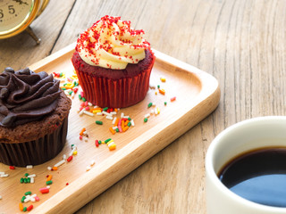 Red and chocolate cupcakes put on a spherical wooden plate. Beside of cupcake have Cactus and white coffee mug.All of it rests on wooden table.