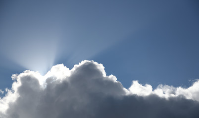 sun rays shining from behind a thick cloud on clear blue sky