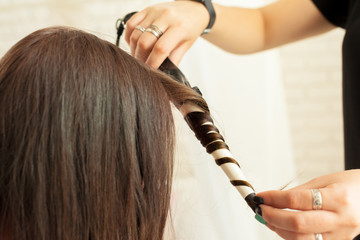 Fototapeta premium Hairstylist curling hair client in hairdressing salon