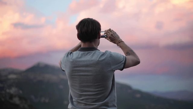 Man tourist traveller makes photos with phone for Instagram social network of clouds in top mountains slow motion close-up from back and side view. Connection communication 4g internet travel concept