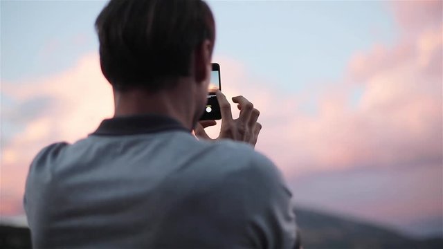 Man traveller makes panoramic photo holding and turning phone standing on top of sunset mountain slow motion close up from back and side view. Technology travel fast mobile internet network connection