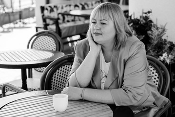 Cheerful plump lady is sitting at the table in cafe and drinking tea. Young pretty funny woman having lunch at a cafe on the street