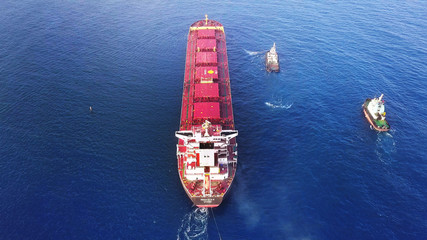 Large bulk carrier ship pulled by tugboats in open water