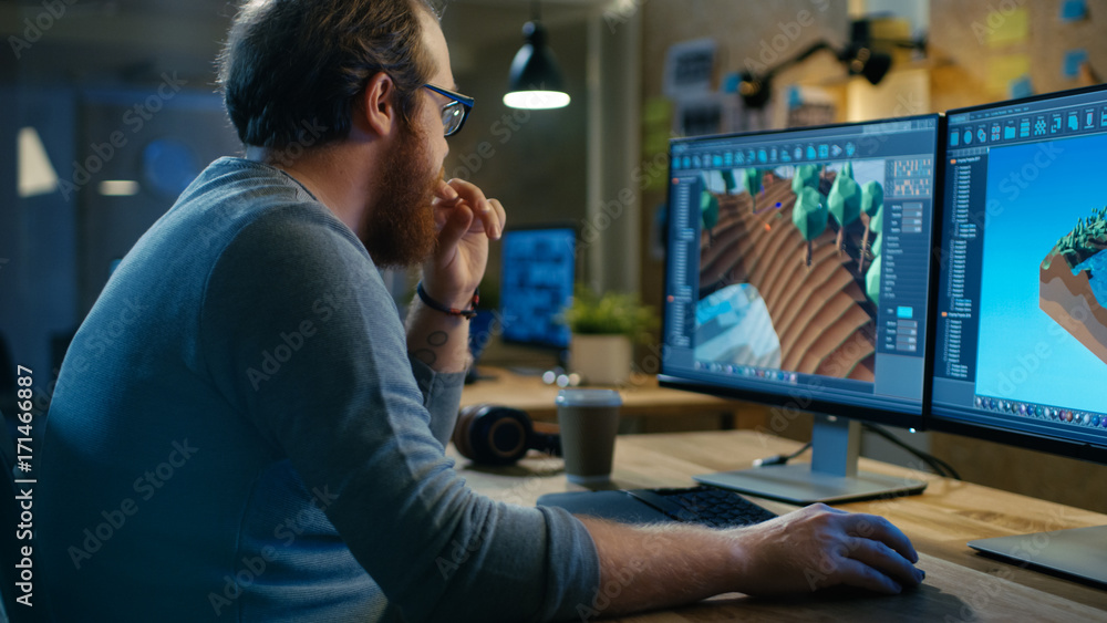 Poster Creative Male Game Developer Works with Graphics for the New Level Design, He Sits at His Wooden Table Working on Two Display Personal Computer. Other People Work in This Creative Studio.