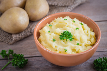 Mashed potato in bowl and fresh potatoes on sackcloth