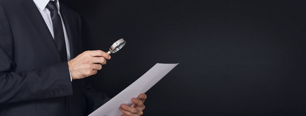 suit man examines document with magnifying glass