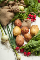 Radishes, potatoes and onions on a white wooden background