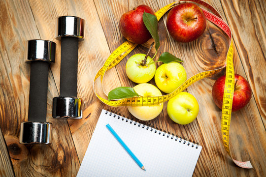 Apples, diet plan and centimeter, dumbbells on a wooden background