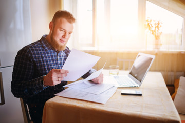 Businessman at home, he is working with a laptop, checking paperwork and bills