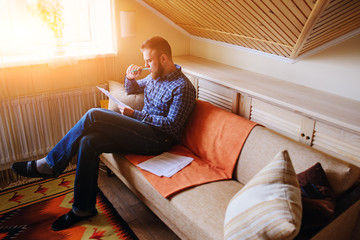 Obraz premium Young handsome man sitting on the couch and watches a working paper
