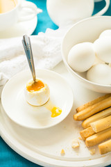 Traditional breakfast: soft-boiled eggs, green tea and bread sticks on white wooden desk. Selective focus