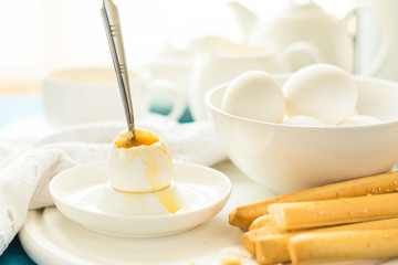 Traditional breakfast: soft-boiled eggs, green tea and bread sticks on white wooden desk. Selective focus