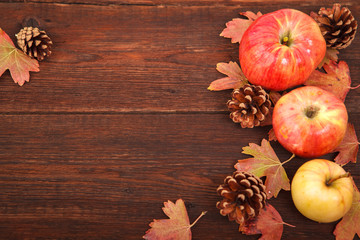 Autumn concept, fallen red-yellow currant leaves with apples and pine cones on a wooden table. Thanksgiving Day.