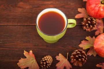 Autumn concept, fallen red-yellow leaves with apples, pine cones and a cup of tea on a wooden table. Thanksgiving Day.