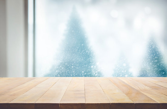 Wood table top on blur window view with pine tree in snow fall of morning winter season.For christmas day background and new year concept