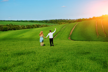 Young happy lovers running on meadow with green grass and blue sky, From the back