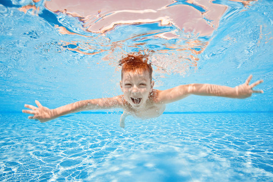 Happy young boy swim and dive underwater, kid breast stroke with fun in pool. Active healthy lifestyle, water sport activity and lessons with parents on summer family vacation with child