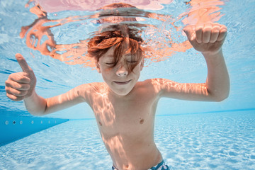 Obraz na płótnie Canvas Happy young boy swim and dive underwater, kid breast stroke with fun in pool. Active healthy lifestyle, water sport activity and lessons with parents on summer family vacation with child