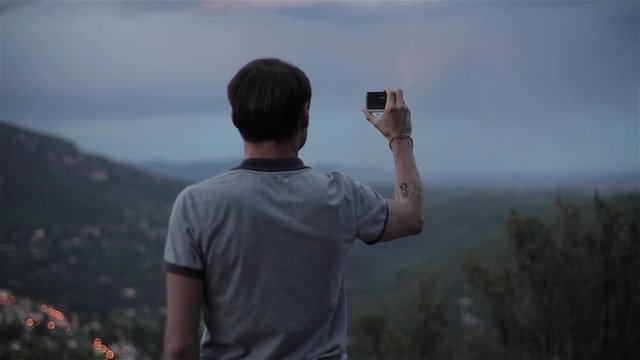 Man shoots with gopro in mountains slow motion close-up rack focus. Male traveller explorer makes video of picturesque evening hills valley in Europe with small camera for lifestyle experience vlog