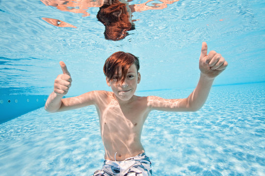 Happy young boy swim and dive underwater, kid breast stroke with fun in pool. Active healthy lifestyle, water sport activity and lessons with parents on summer family vacation with child