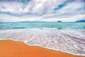 Sunny sandy beach with wave foam at turquoise sea water and epic cloudy sky background. Greece.