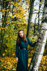 Beautiful girl in a green dress among the fallen leaves in the forest. Autumn.