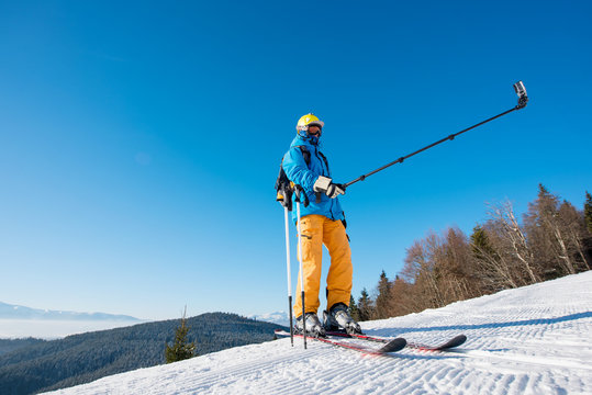 Full length shot of a skier standing on top of a mountain on a sunny winter day taking a selfie with a camera on monopod at the winter resort copyspace technologies memories selfie stick concept