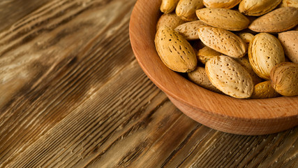 Raw almond in wooden bowl in the corner of rustic kitchen table. Organic background