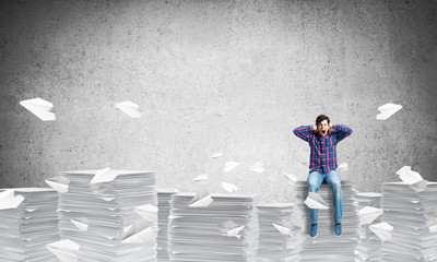 Attractive man sitting on pile of paper documents.