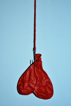 deflated heart-shapped balloon hanging from a hook upside down on a blue wall