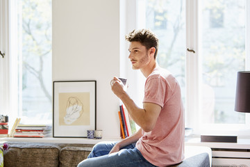 Young Man Having Coffee On Sofa In Living Room