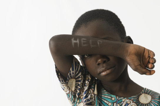 Littel African boy asks for help by covering his face with his arm, isolated on white