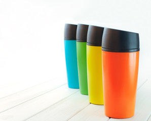 Color thermos mugs on white wooden table on white background