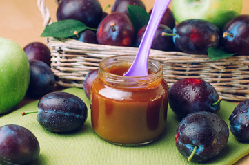Jar with baby food plum puree with spoon near fresh plums